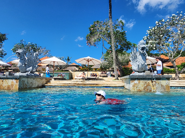 수영장에 흰 모자와 선글라스를 쓴 사람이 수영을 하고 있다.