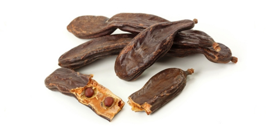 주엽나무의 열매인 조각을 하얀 바닥에 여러 개 놓아두고, 그 중에 한 개는 껍질을 까서 속에 씨앗이 보이게 놓아두고 찍은 사진