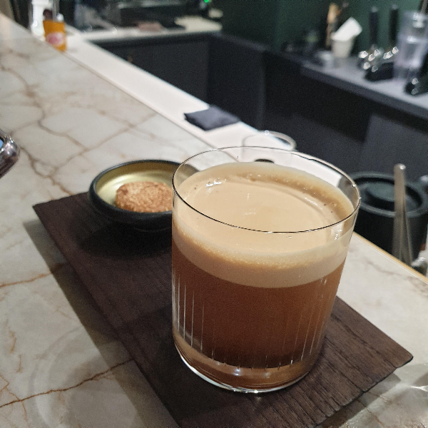 나무 쟁반 위에 거품이 있는 아이스 아메리카노와 디저트가 같이 올려져 있다.