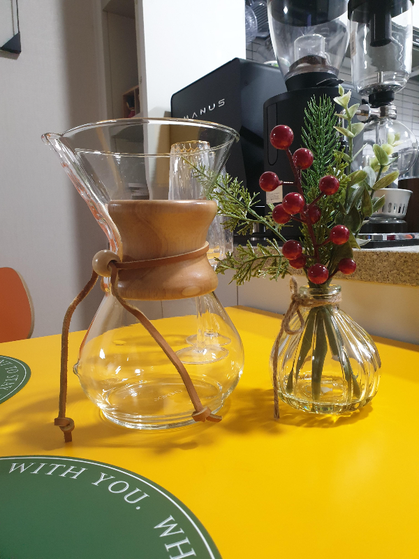 케멕스 드리퍼와 꽃병이 노란 테이블 위에 올려져 있다.