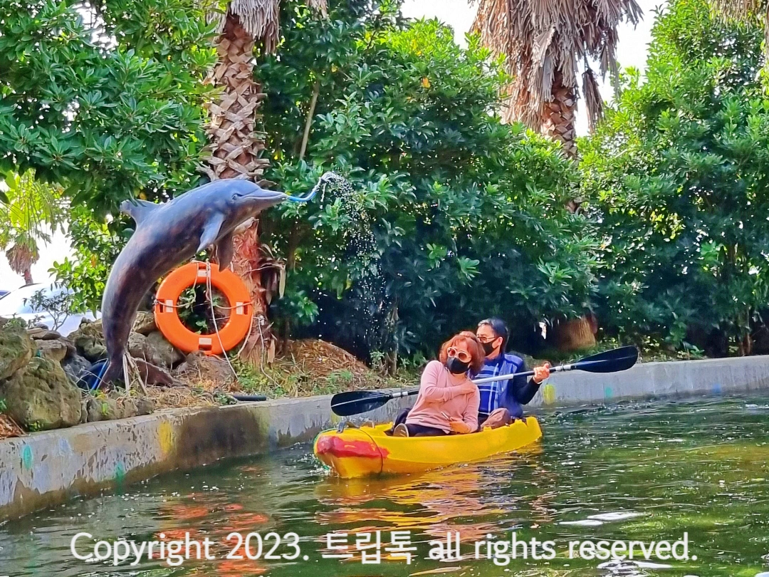 돌고래 조형물 입에서 물이 뿜어져나오고 노란 카약을 탄 사람들이 황급히 피한다.