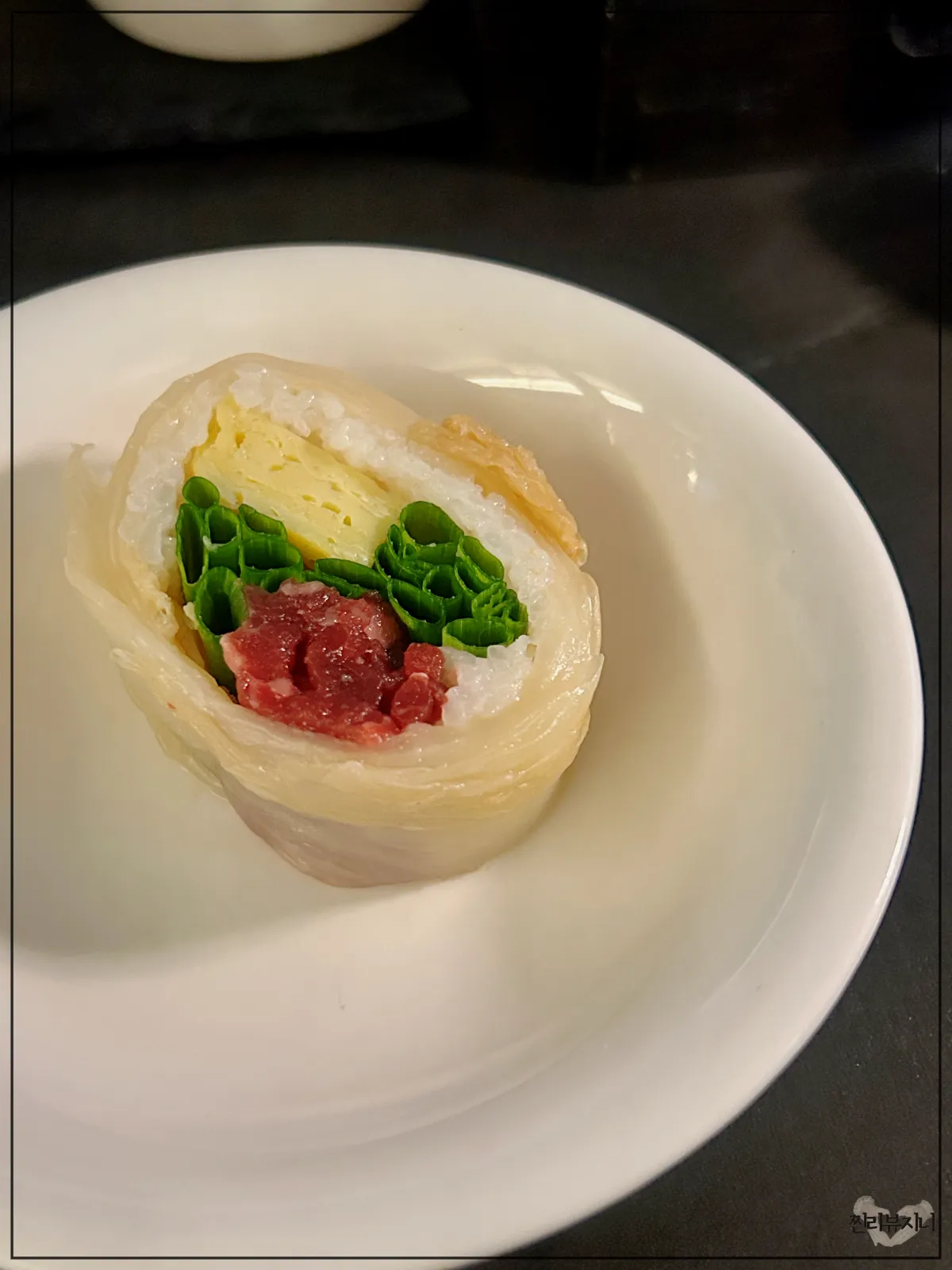 묵은지로-감싸진-육회-마끼-1개가-접시-위에-올려진-사진