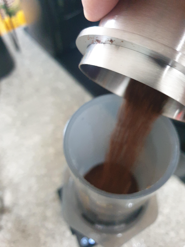 테이블에 에어로프레스가 올려져있고 에어로프레스에 원두를 붓는 모습