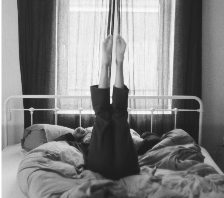 침대 위에서 다리를 들어 올리며 아침 스트레칭을 하는 사람의 모습. 흐트러진 주말 리듬을 회복하며 하루를 시작하는 장면.