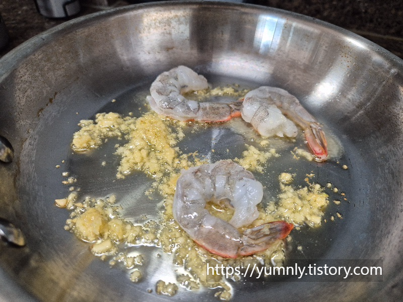 Adding three fresh shrimps to the pan with sautéed garlic.