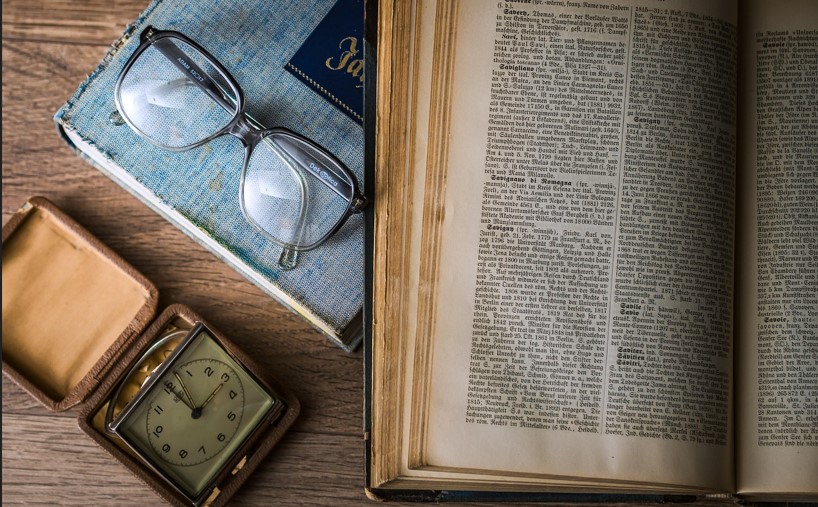 오래된 책이 펼쳐져 있고 그 옆에 안경과 시계가 놓여있는 사진