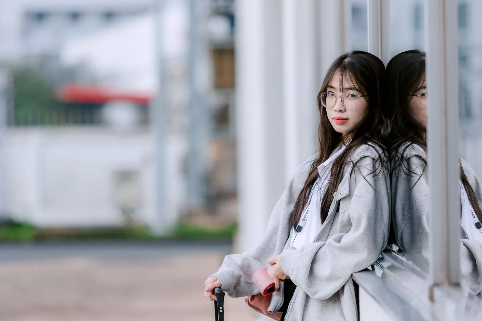 회색 재킷을 입은 세련된 젊은 여성이 유리창에 기대어 고요한 명상에 잠겨 있는 모습입니다.