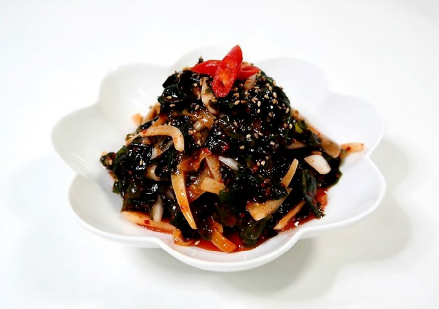 바다에서 채취를 한 미역을 살짝 삶은 후에 식초와 양파와 버무려 무친 미역초무침을 하얀 바닥 위에 유리 그릇에 수북하게 담아 놓은 후에 찍은 사진