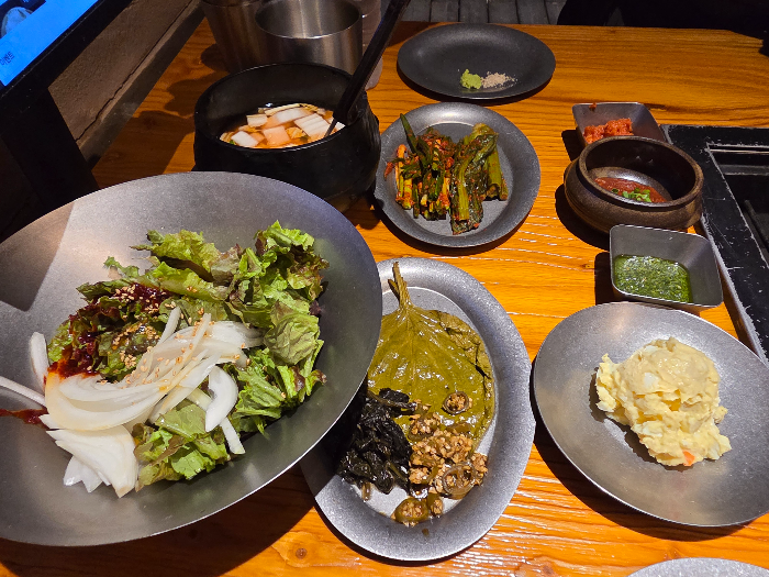 밑반찬이다. 깻잎, 감자샐러드, 물김치, 갓김치 등이 보인다.