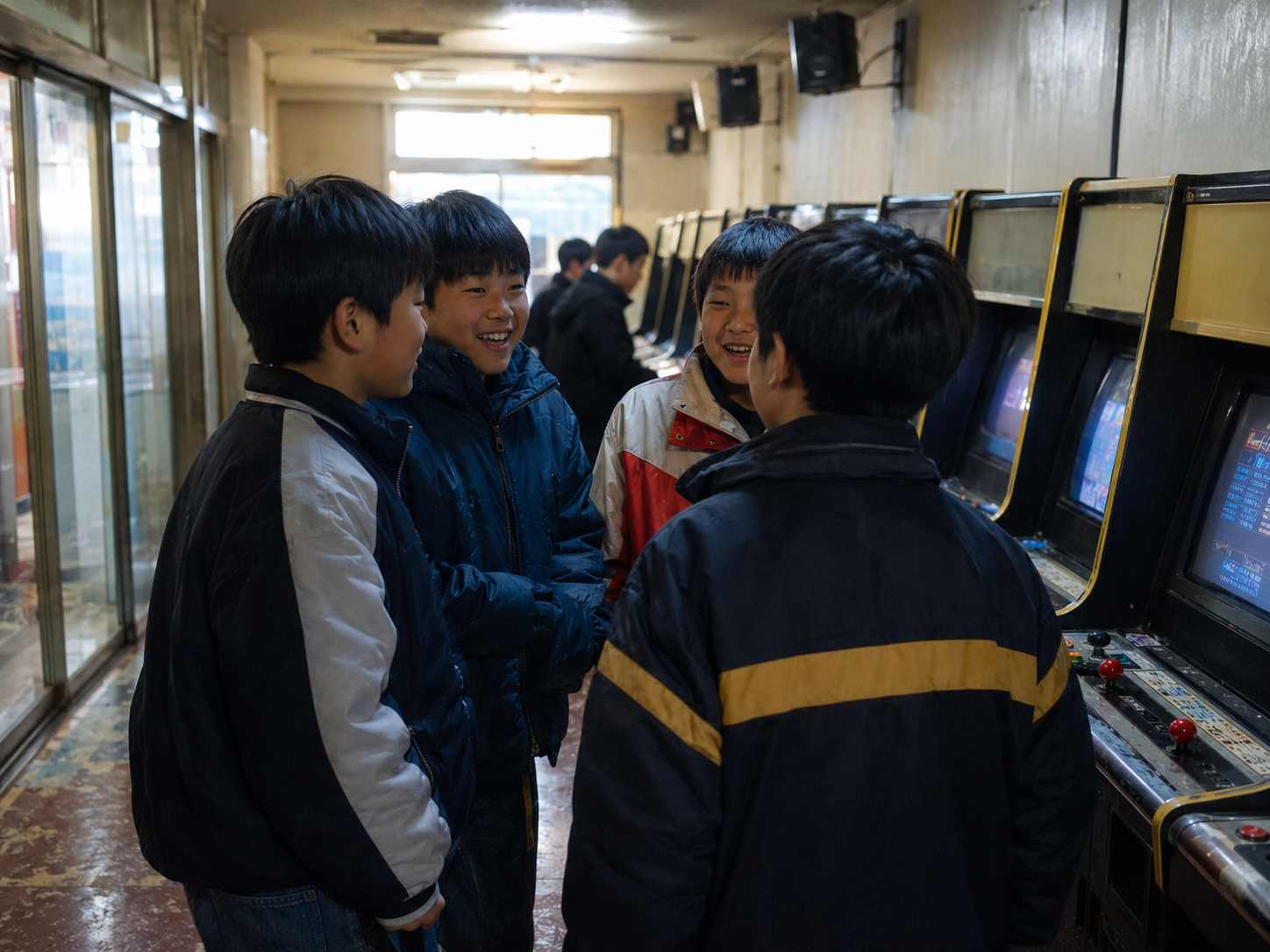 오래된 아케이드 게임기가 있는 동네 오락실에서 여러 아이가 모여 이야기를 나누는 모습