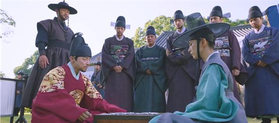 두 사람이 앉아서 바둑을 두고 여러 사람이 구경하고 있다