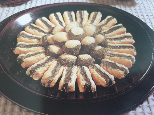 검정색과 진한 적색으로 멋을 낸 접시에 거피팥과 쑥으로 겹겹이 모양을 낸 쑥굴레가 담겨있는 모습