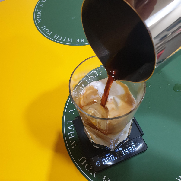 얼음과 우유가 담긴 컵에 추출한 커피를 스팀피처를 이용해 넣고 있다.