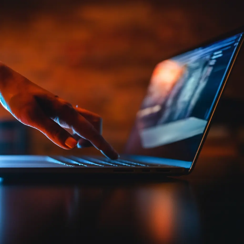 어두운 조명 속에서 노트북을 조심스럽게 조작하는 손을 클로즈업한 이미지 – 사적인 기록과 디지털 프라이버시를 상징적으로 표현