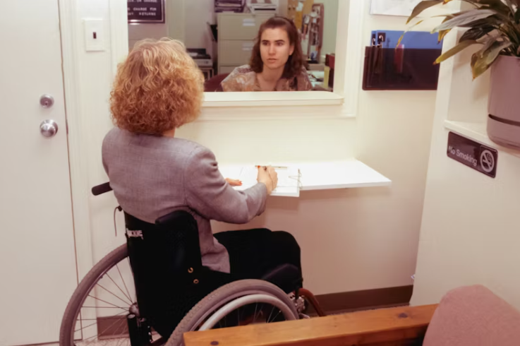 휠체어를 탄 여성이 병원 접수창구에서 상담 중인 모습. 의료비 지출과 관련된 서류를 작성하는 장면