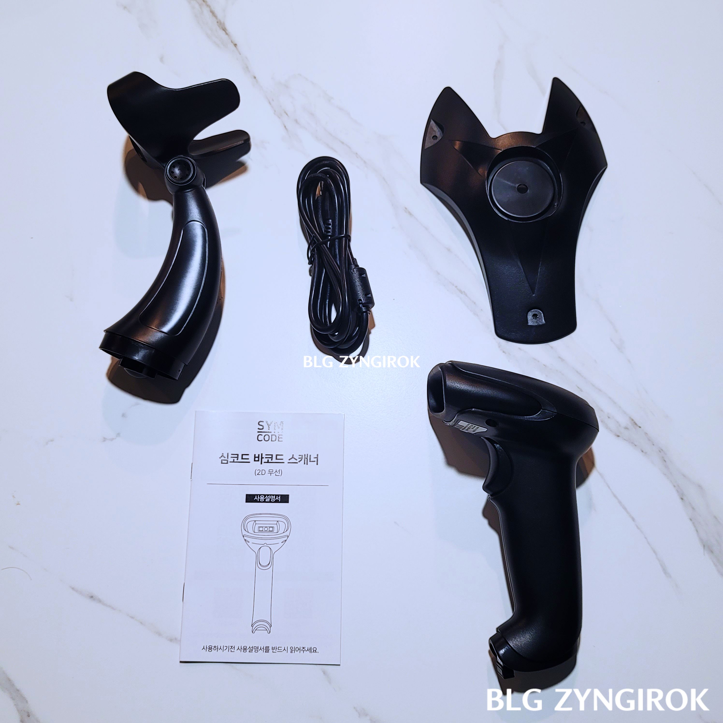 심코드-바코드-스캐너-구성품들이-놓여있다.-거치대-usb-케이블-거치대의-지지대-설명서-그리고-본체가-순서대로-놓여있다.
