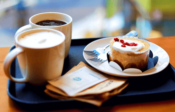 테이블 위에 스타벅스 아메리카노 커피와 카페라떼 2잔이 있고 동그란 케이크도 있다.