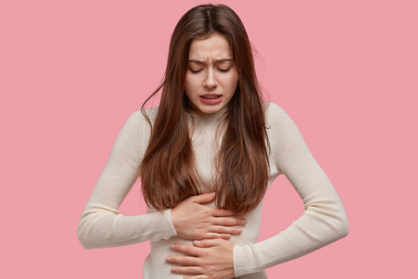 배가 아픈듯 배를 움켜잡고있는 여성의 사진