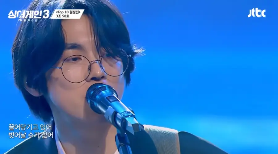 싱어게인3-
파란배경의 무대 앞으로 자연스럽게 내려온 웨이브진 머리 검은테 안경 스탠딩 마이크에 입을 대고 눈을 그윽하게 뜬채 노래하는 58호