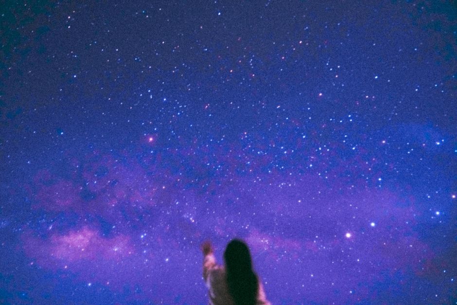 A silhouette of a person reaching towards a vivid starry night sky, featuring the Milky Way.