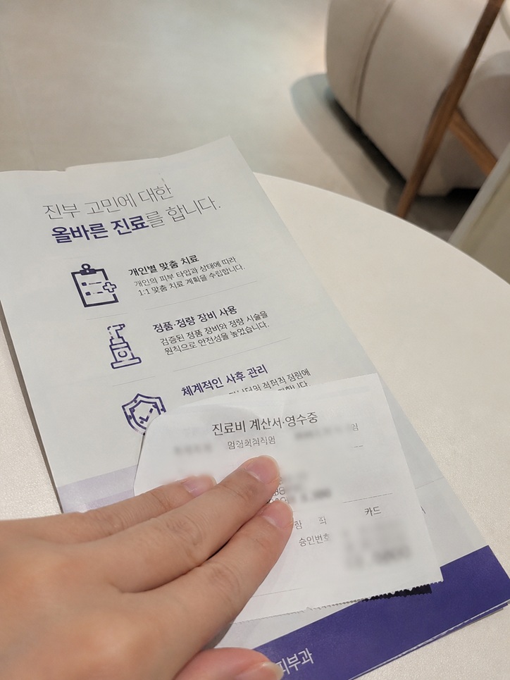 피부과 원형 테이블 위에 놓인 진료 안내 팸플릿과 손으로 일부를 가린 진료비 계산서 영수증 실제 사진