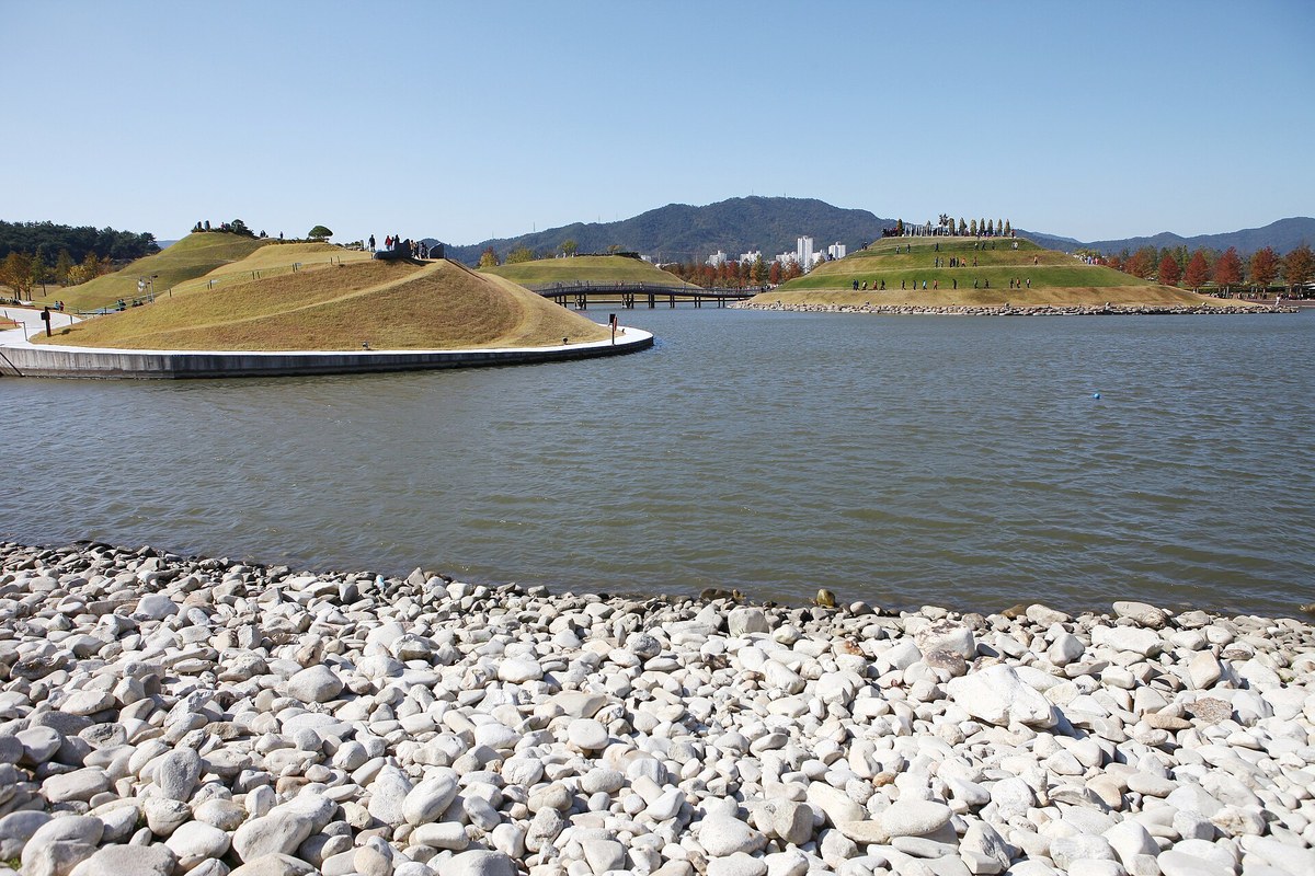 Grassy mounds and a footbridge across the lake at Suncheon Bay National Garden in autumn