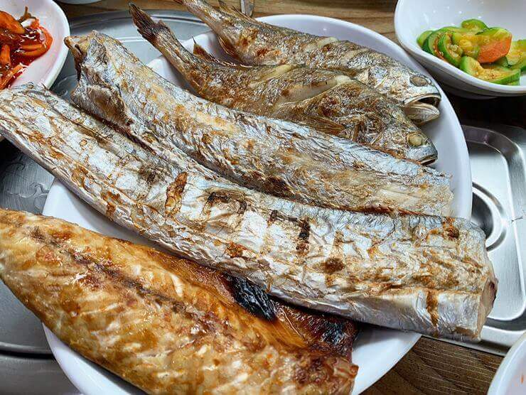 생선구이 사진이다. 고등어, 갈치 2조각, 조기 2마리가 접시에 나란히 놓여 있다.