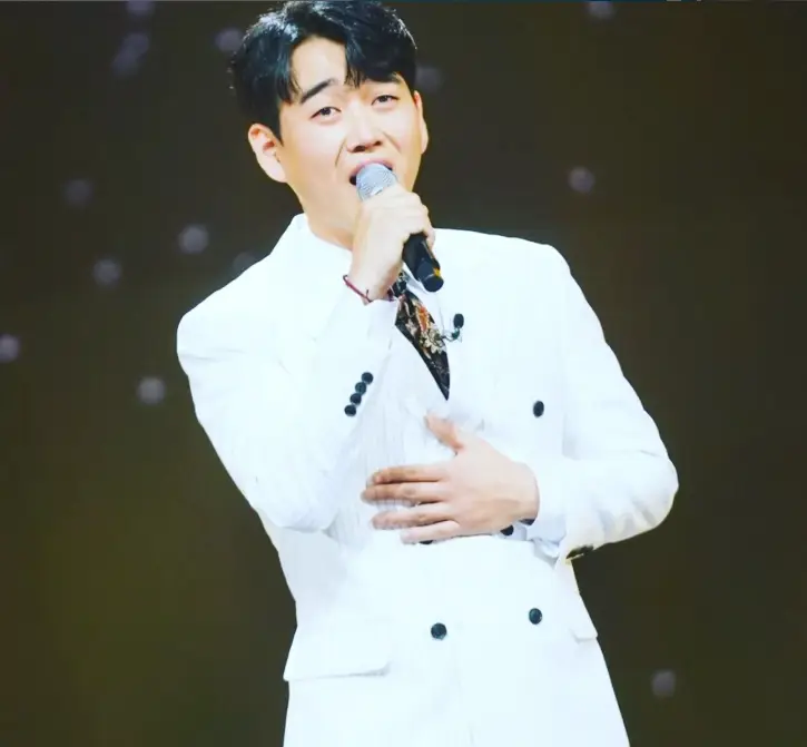황영웅- 검은배경 흰수트를 입고 오른손에 마이크를 든채 노래하는 황영웅