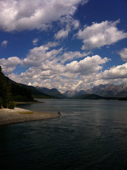 구름이 가득한 하늘 아래 광활하게 펼쳐진 호수와 산맥, 호숫가에 선 두 사람.