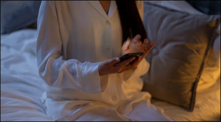 침대에 앉아 스마트폰을 확인하는 모습