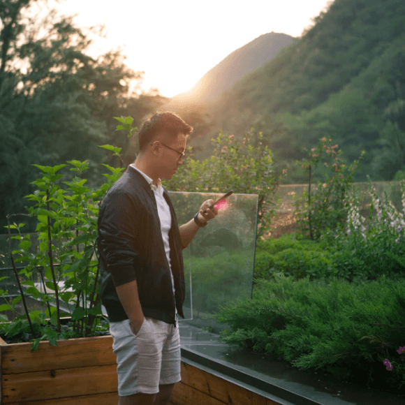 남자가 핸드폰 들고 햇빛 받는 사진