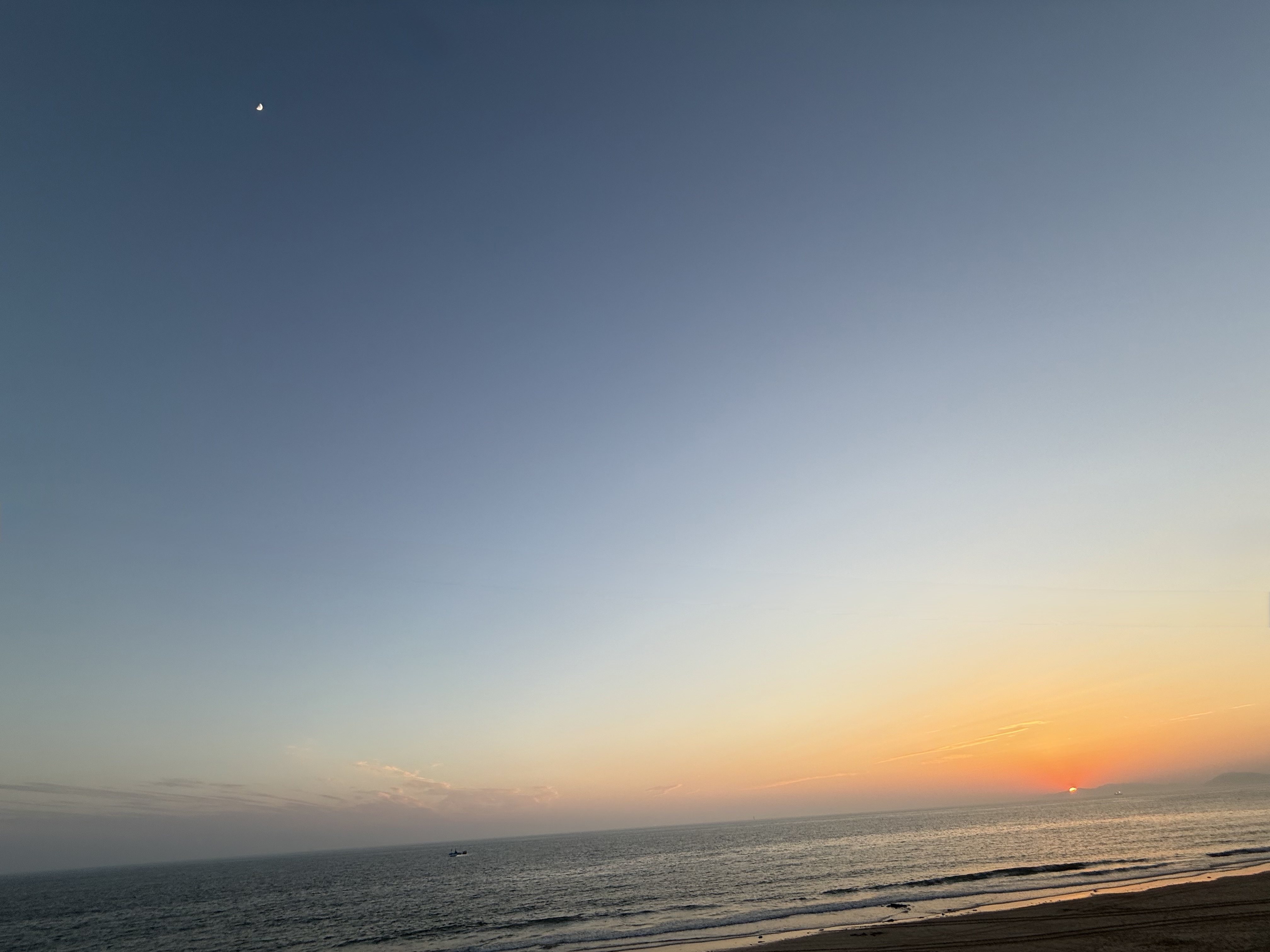 바다 수면위에 해는 절반 걸쳐 있고 그 위로 반달이 떠 있는 모습입니다.