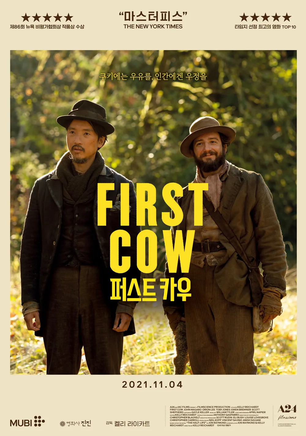 가을빛이 물든 숲속 배경 앞에 두 남자가 나란히 서 있는 영화 <퍼스트 카우> 포스터. 왼쪽에는 중절모를 쓴 중국계 남성 킹 루가, 오른쪽에는 수염이 있는 백인 남성 쿠키가 중절모와 낡은 작업복 차림으로 서 있다. 두 사람은 온화한 표정으로 관객을 바라보며, 중심에는 노란색으로 &ldquo;FIRST COW 퍼스트 카우&rdquo;라는 타이틀이 크게 적혀 있다. 상단에는 &ldquo;마스터피스 &ndash; THE NEW YORK TIMES&rdquo;와 &ldquo;제86회 뉴욕 비평가협회상 작품상 수상&rdquo; 등의 찬사가 인쇄되어 있다. 하단에는 개봉일 "2021.11.04"가 명시되어 있다.