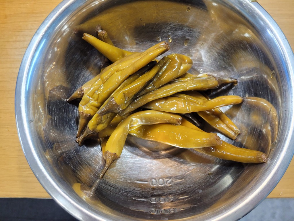 노란빛이 도는 통 고추 장아찌를 볼에 담은 모습