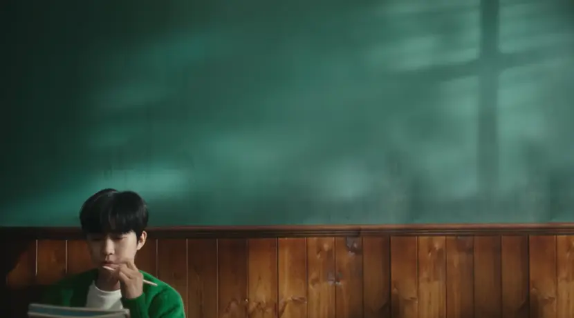 임영웅- 초록 벽지 아래 갈색 나무벽 좌측 하단 초록 가디건 안 흰 티를 입은 임영웅이 왼손으로 연필을 들고 생각하는 모습