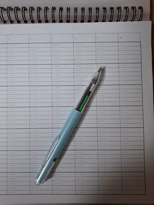 사용자가 루틴을 체크하기 위해 직접 정성스럽게 칸을 그어놓은 노트와 볼펜 (A notebook and a ballpoint pen where the user has carefully drawn cells to check routines)