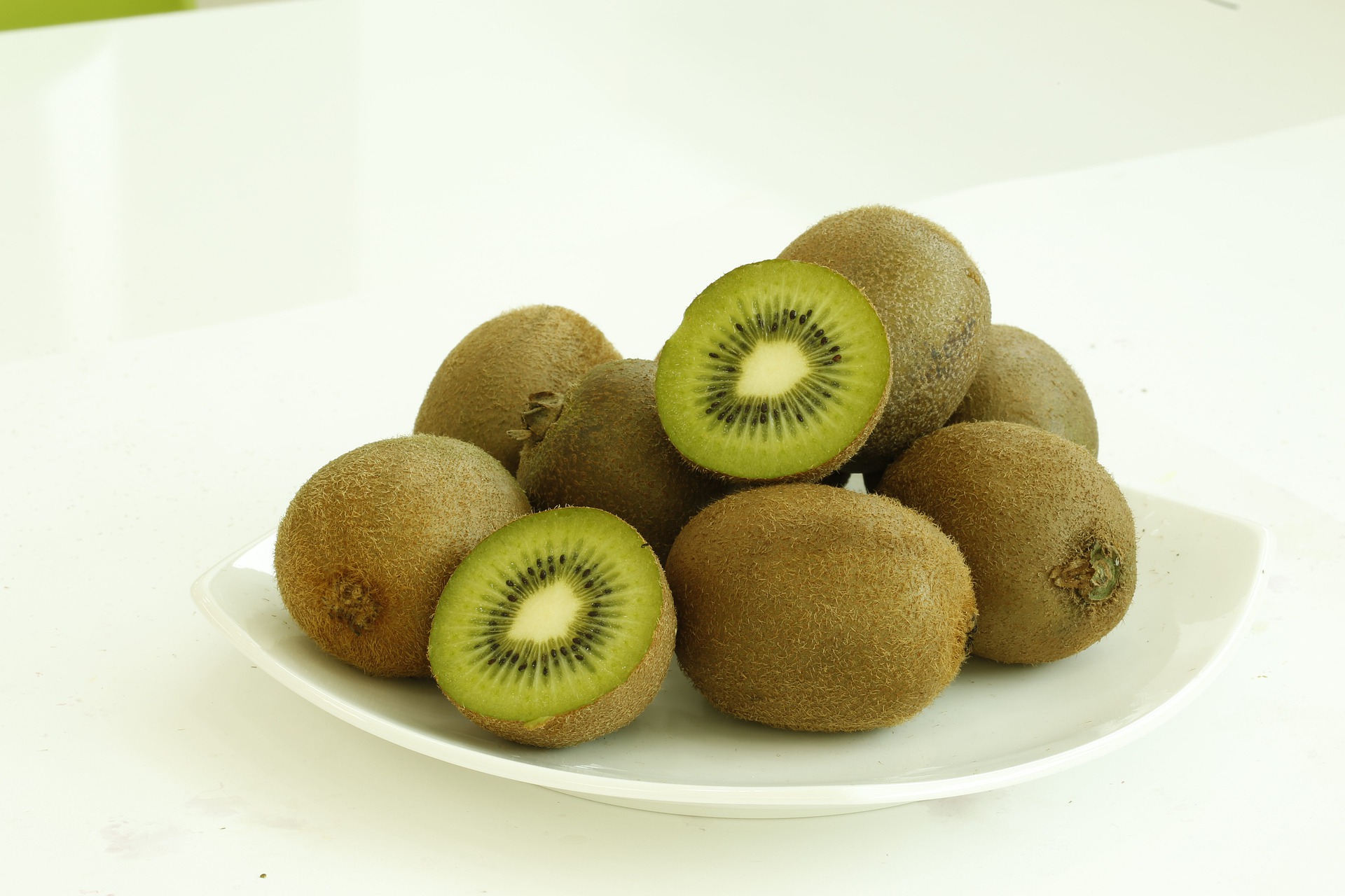 야생의 키위나무에서 채취를 한 키위 열매를 깨끗이 세척을 해서 하얀 바닥 위의 네모난 유리 접시 위에 키위을 8개 정도 놓아두고, 그 중에 한 개는 반으로 잘라서 속이 잘 보이게 놓아 둔 사진