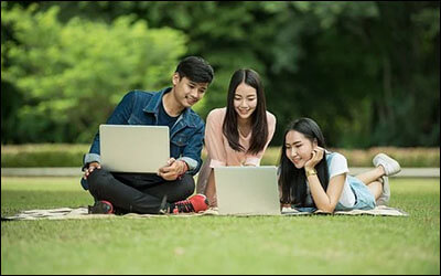 학생 셋이 잔디 위에서 노트북을 보며 이야기하고 있는 모습