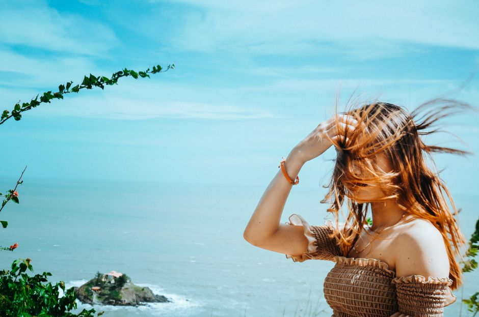 Woman in off-shoulder dress enjoying a breezy day by the beach with ocean views and wind-swept hair.