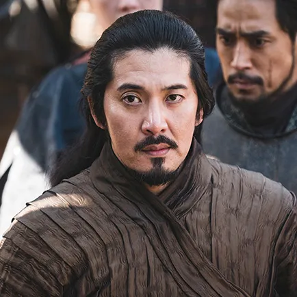 군대를 배경으로 짙은 갈색 무복을 입고 머리를 뒤로 묶은 아라문의 검 소당 캐릭터