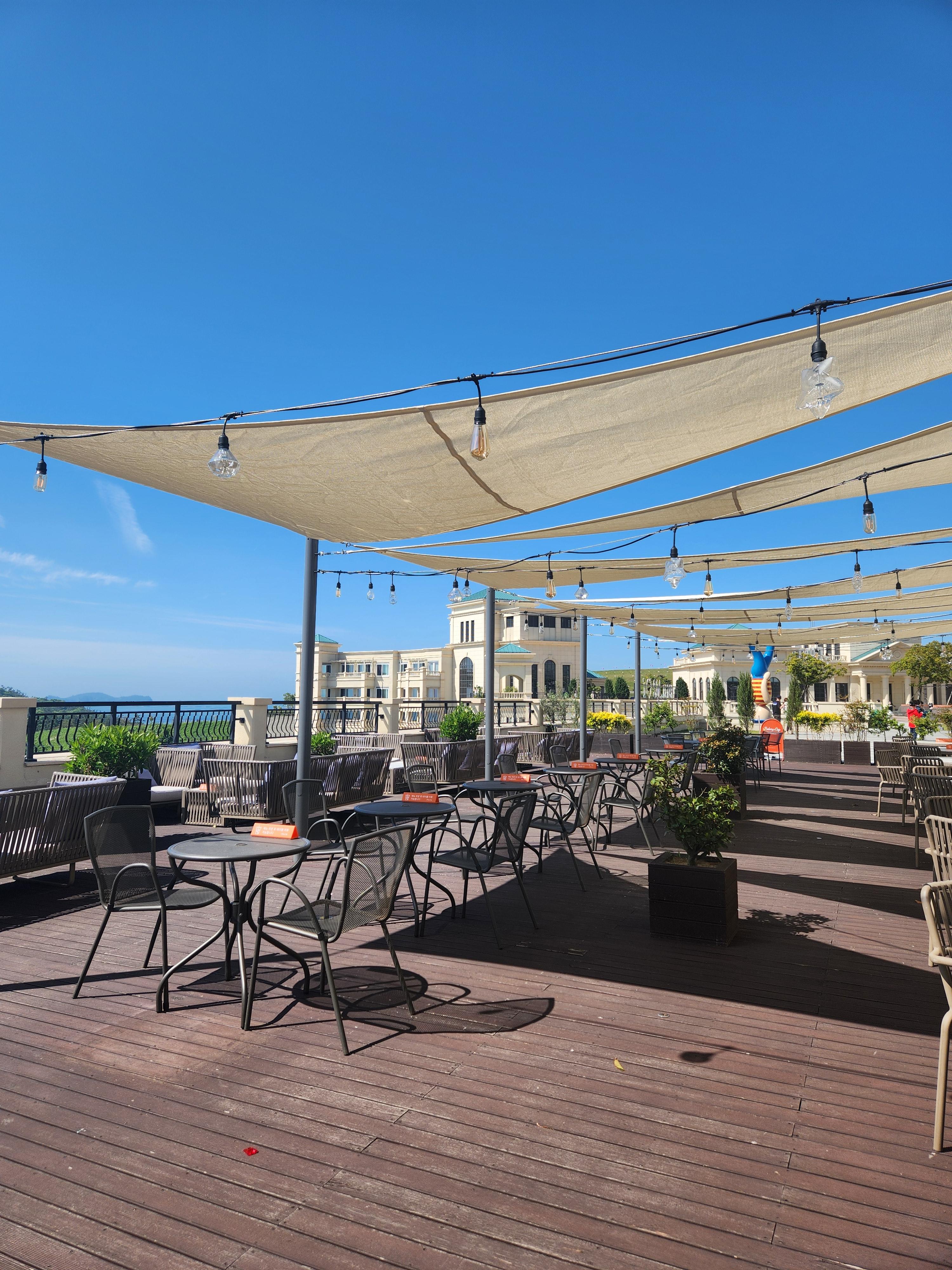 까페 테라스-유럽 지중해 분위기가 나는 테이블과 의자-햇빛을 가리는 삼각 그늘막-푸른 바다와 하늘