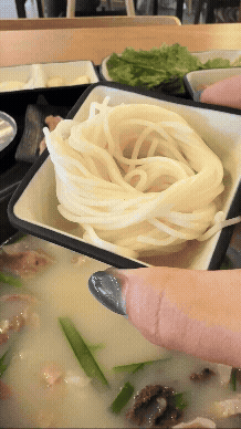 경자국밥 섞어국밥 뚝배기 위로 소면을 담은 그릇을 기울이며 면을 넣는 장면. 하얀 소면이 보글보글 끓는 국밥 위로 떨어지고 있으며, 테이블에는 수육과 밑반찬이 함께 차려져 있다.