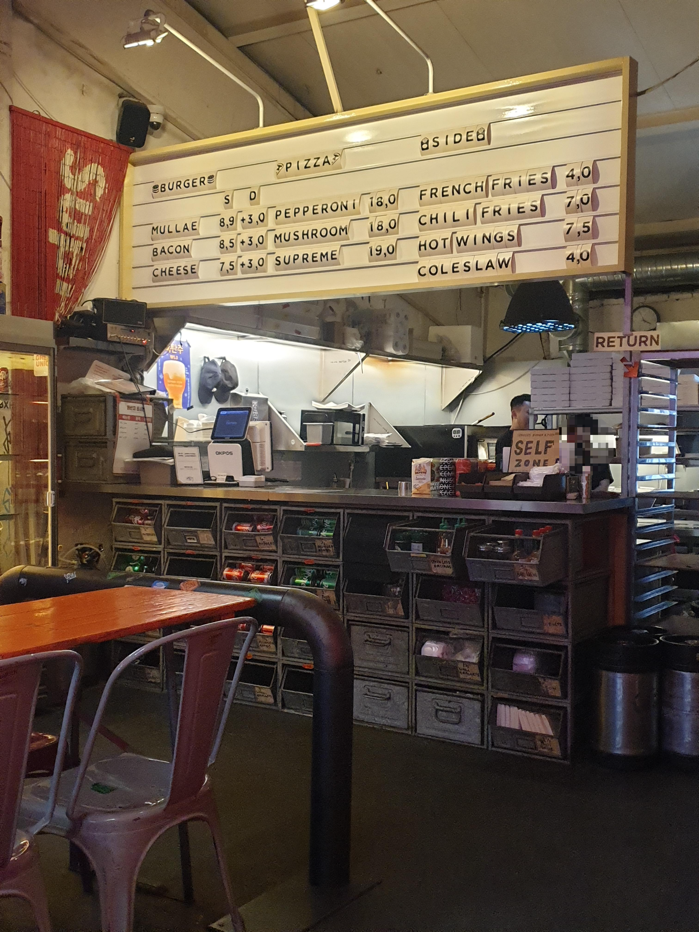 픽업대 위에 메뉴와 가격이 표시되어 있다. 버거와 피자 그리고 사이드 메뉴로 구성