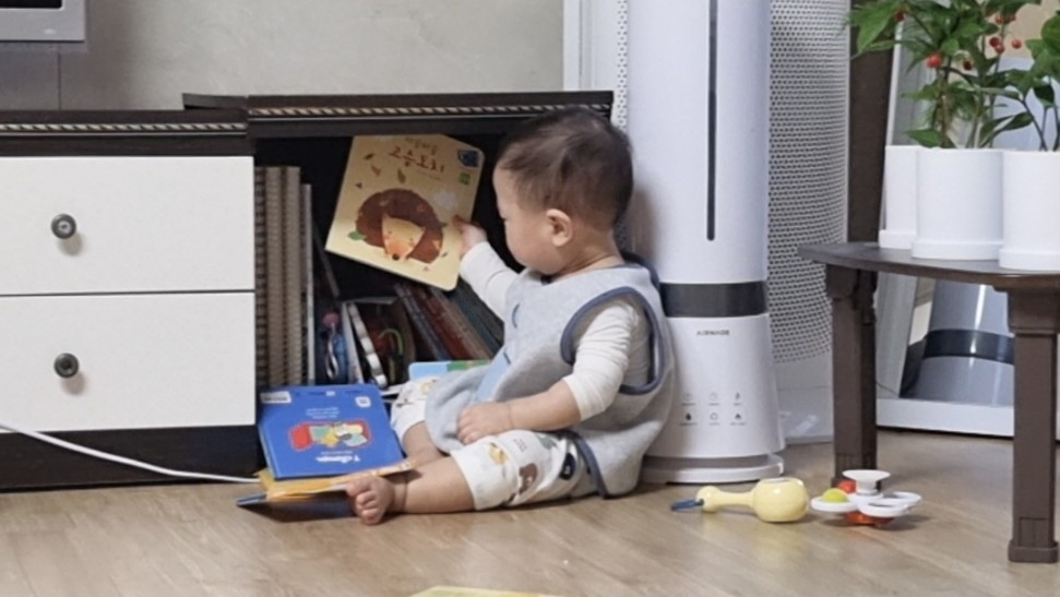 방바닥에 앉아 책장에서 고슴도치 그림책을 집어 올리고 있는 아기의 모습