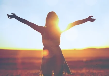 태양을 향해 기뻐하며 두팔을 벌리고 서 있는 여성
