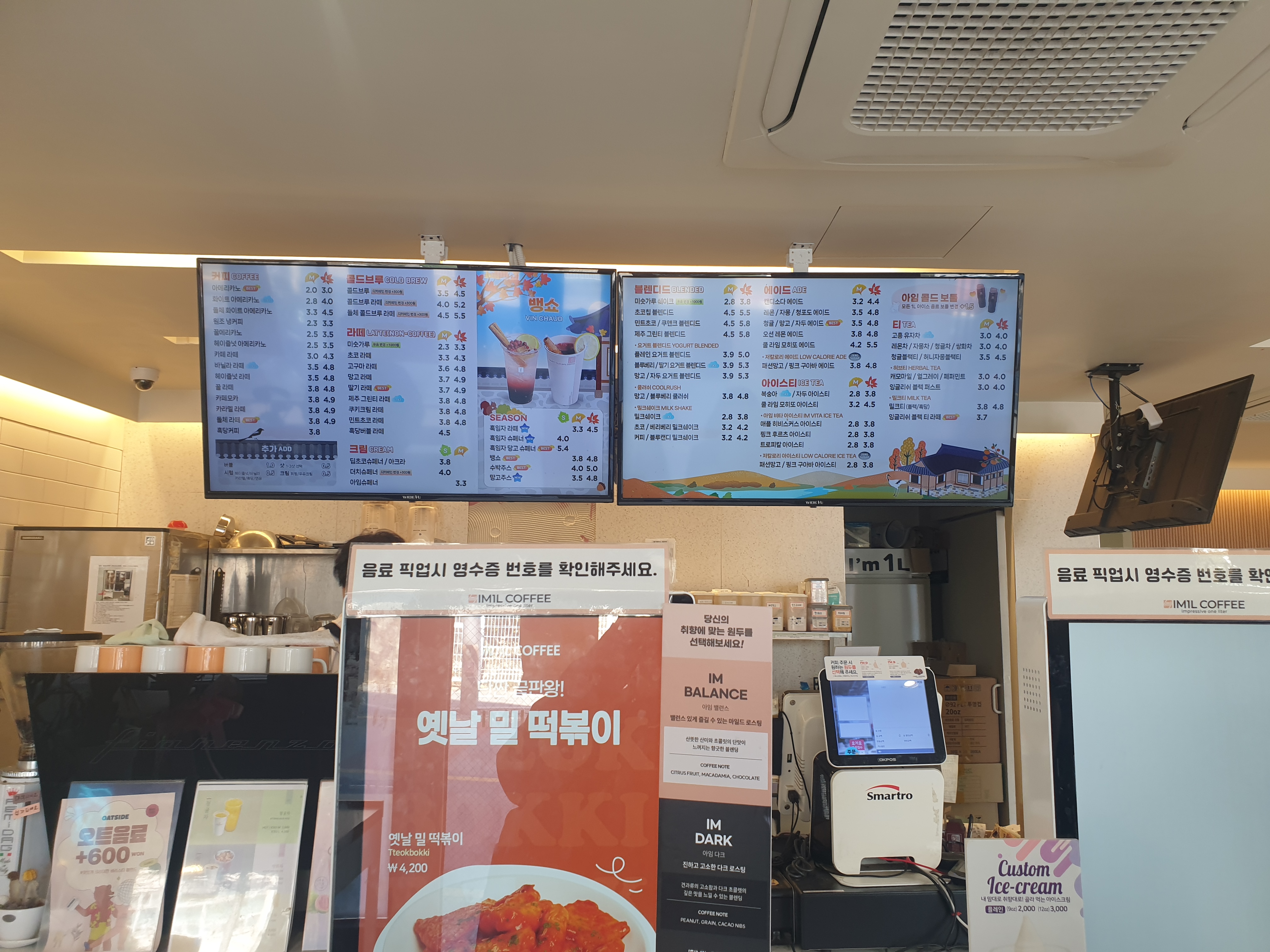 위쪽 모니터에 메뉴가 보이고 앞쪽에는 키오스크 2 대가 있다.