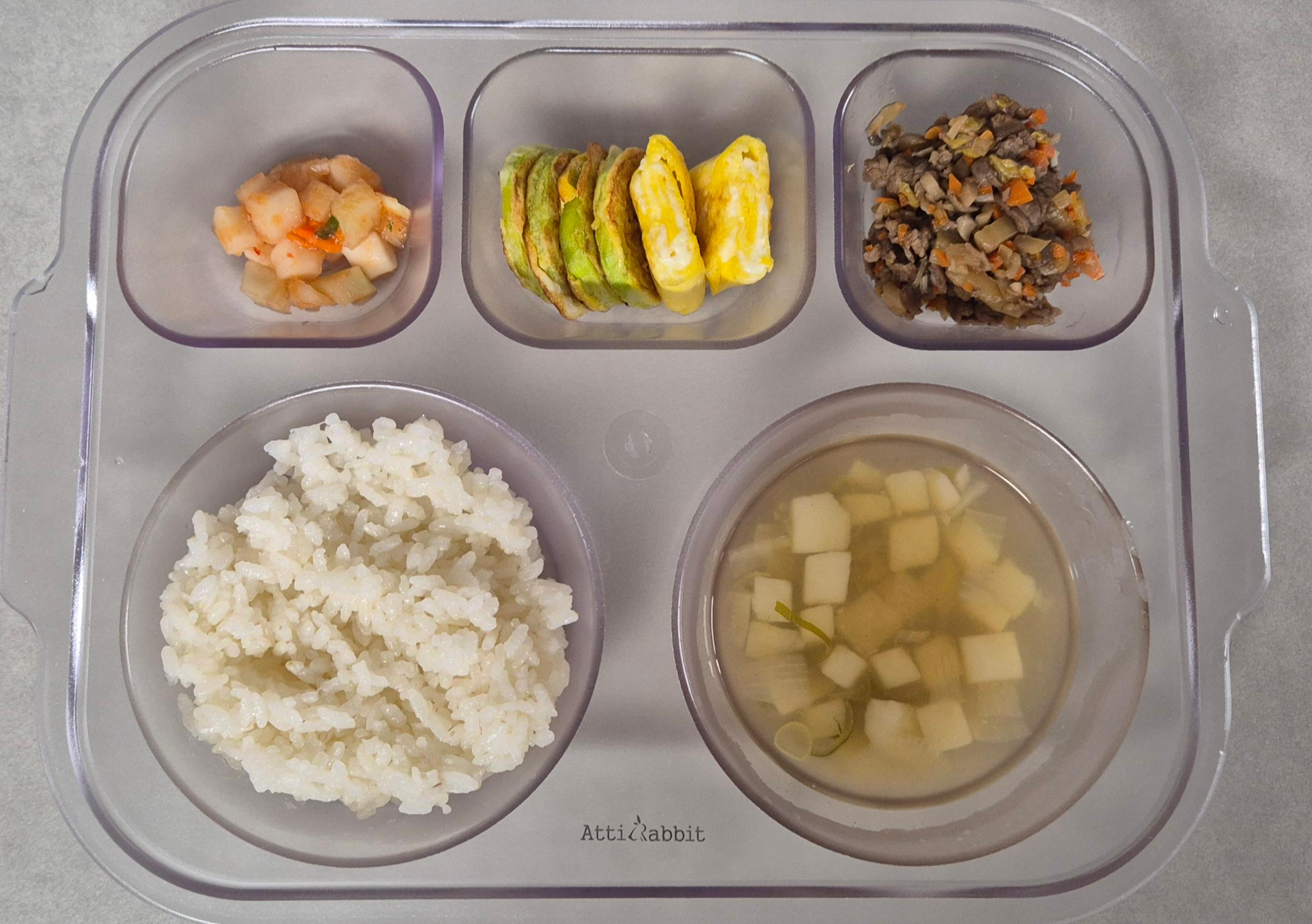 투명한 아기 식판에 담긴 흰쌀밥, 맑은 감자국, 소불고기볶음, 계란말이와 호박전, 아기 깍두기로 구성된 균형 잡힌 유아식단