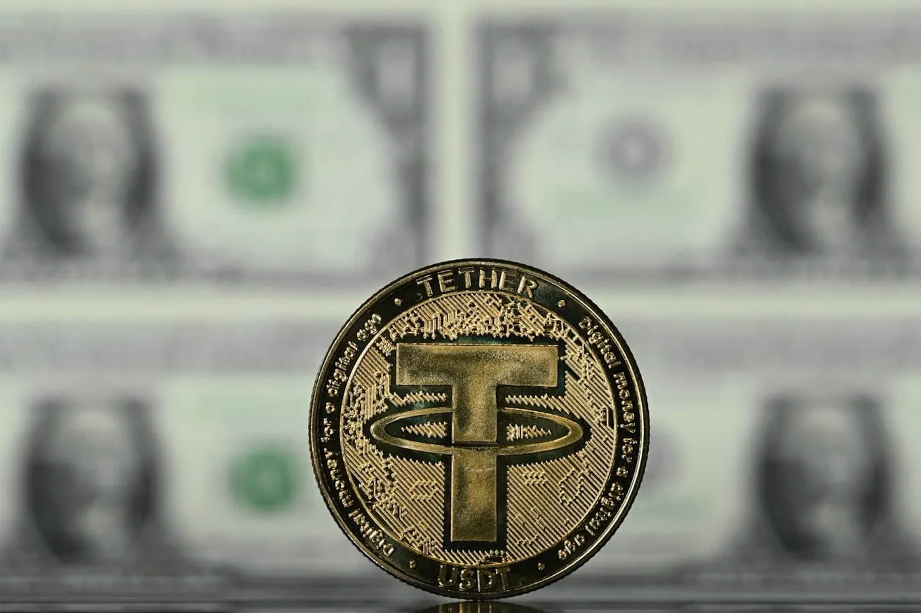 테더(USDT) 금속 동전. 배경의 미국 달러 지폐가 테더 준비금 구조(미국채·달러 담보)를 시각적으로 나타낸다.