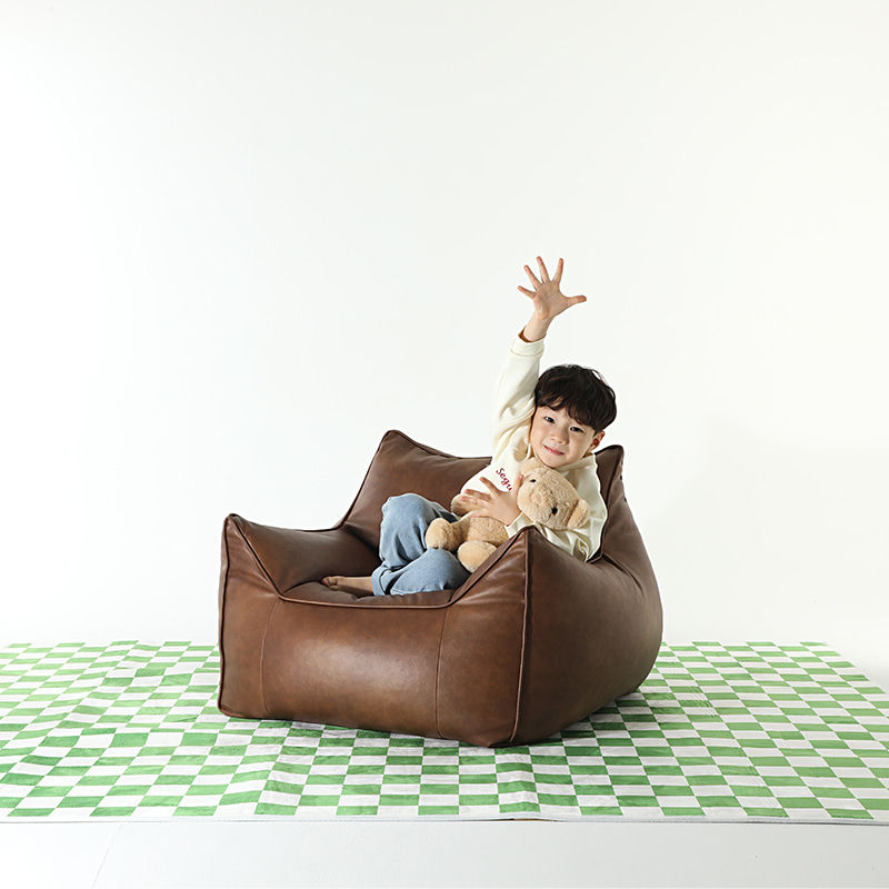 플래지어 톰빈백 미니 기능성 가죽 빈백 소파에 곰인형을 안고 앉아 한 손을 높이 든 아이, 바닥에는 초록 체크무늬 러그