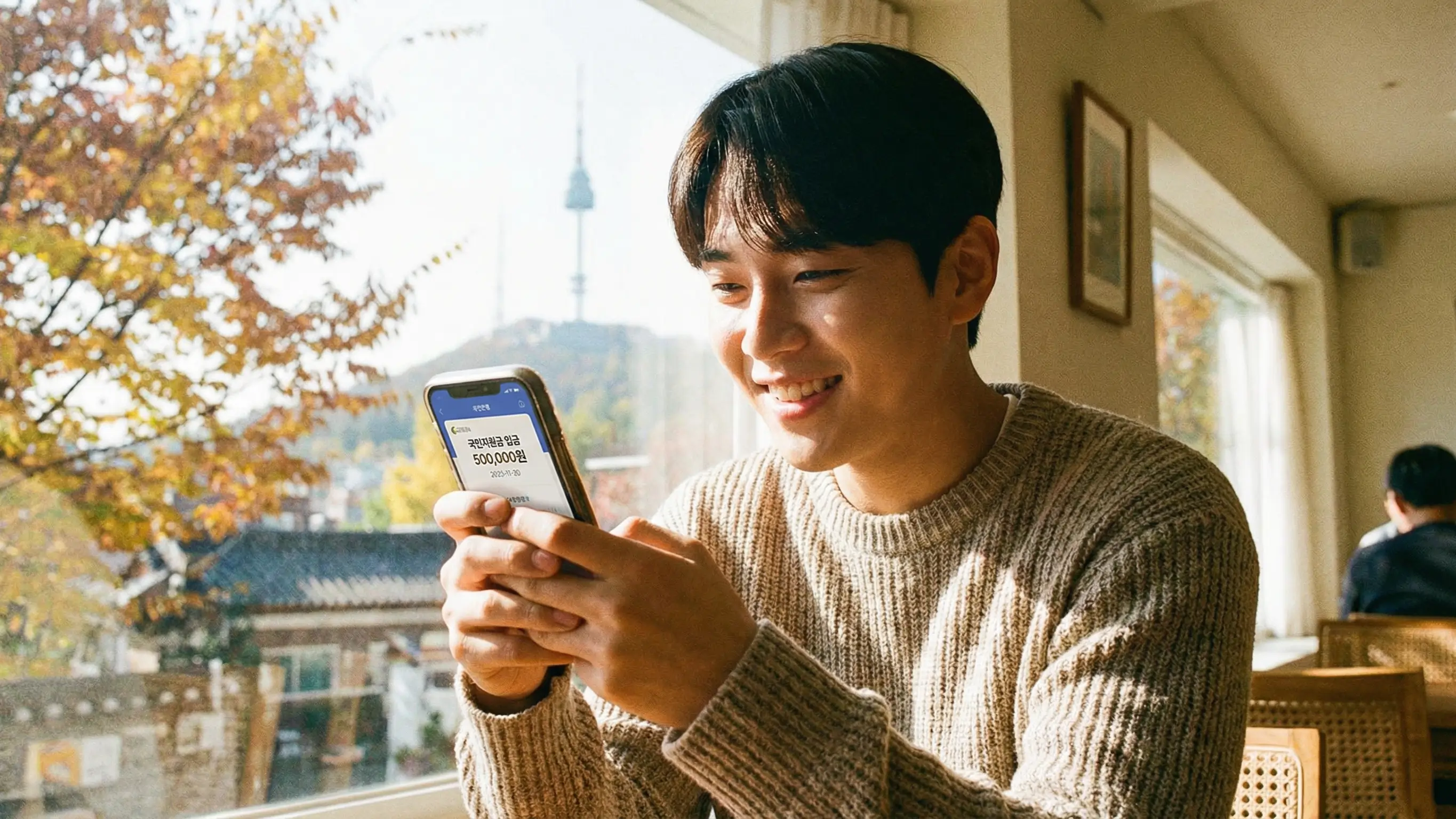 스마트폰으로 지원금 입금 내역을 확인하고 안도하는 한국인 청년의 모습, 희망적인 분위기